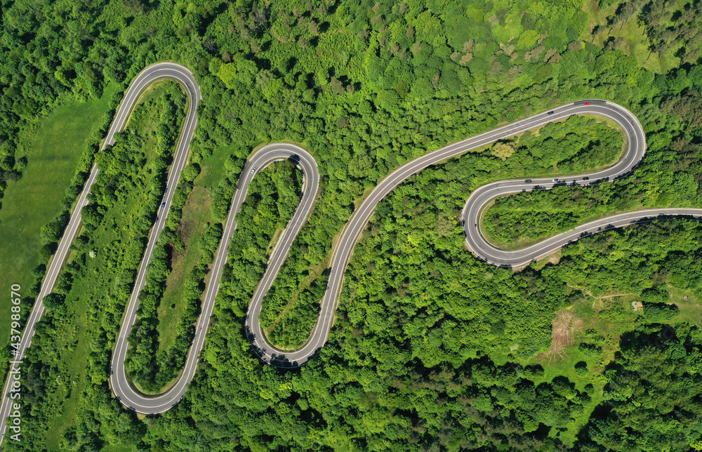 Aerial drone view of winding road between green forest