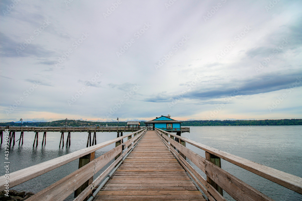 Fototapeta premium Wooden pier at Campbell River, Vancouver Island, BC. The view on the pier, blue house, dark ocean and cloudy sky.