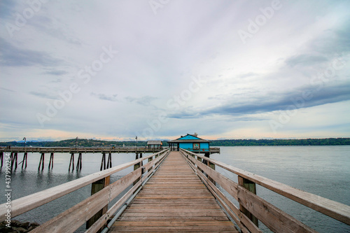 Wooden pier at Campbell River, Vancouver Island, BC. The view on the pier, blue house, dark ocean and cloudy sky. © Klara