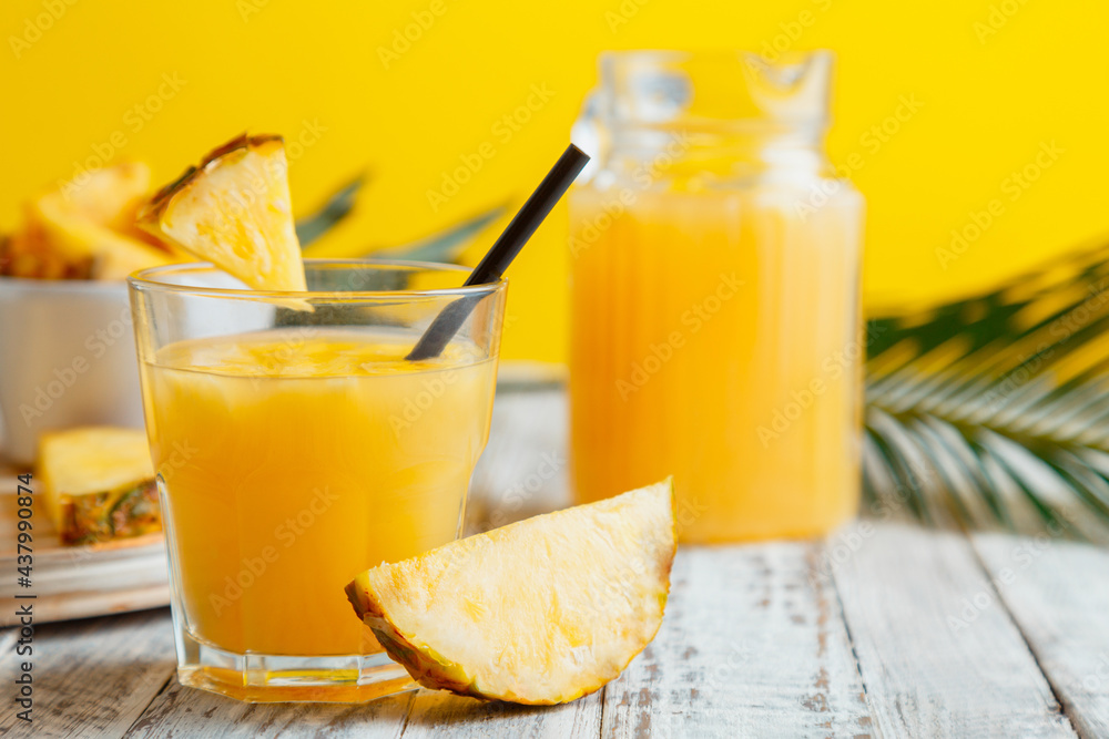 Tasty pineapple juice in glass with ingredients. Fresh natural pineapple juice cocktail and pineapple juice in Glass Jug on white wooden table with yellow summer background palm leaves Tasty pineapple juice in glass with ingredients. Fresh natural pineapple juice cocktail and pineapple juice in Glass Jug on white wooden table with yellow summer background palm leaves