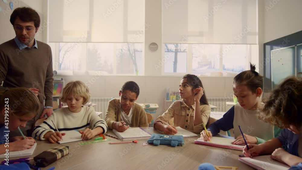 Teacher explaining lesson to schoolchildren. Students writing in exercise books Teacher explaining lesson to schoolchildren. Students writing in exercise books