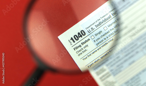 Tax season with magnifying glass, 1040 tax form background, red office desk top view photo