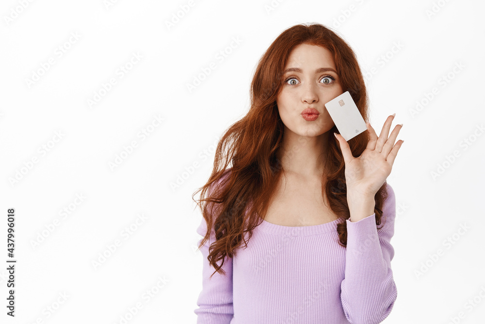 Shopping. Sassy redhead girl pucker lips silly, showing credit card, thinking of going in store, buying something contactless, standing in purple blouse against white background Shopping. Sassy redhead girl pucker lips silly, showing credit card, thinking of going in store, buying something contactless, standing in purple blouse against white background