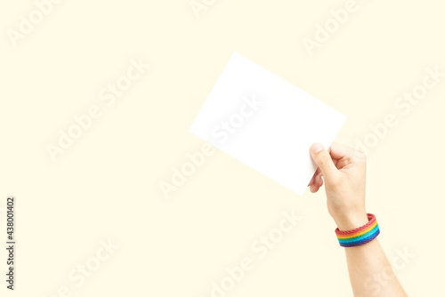 Hand with a rainbow bracelet, LGBT symbol, holding a blank piece of paper
