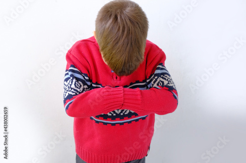 offended or punished child, a boy of 7-8 years old in a red Scandinavian sweater bent down on his face, hunched his back, parenting concept photo
