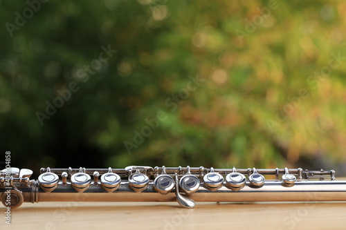 Flute, woodwind brass instrument in classical orchestra. Silver modern flute on white sheet music note for education and performance. Song composer on score sheet with green bokeh nature.