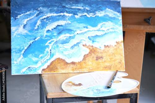 Acrylic sea and beach painting on drawing stand with palette and brush. Blue wave on golden sand hand painting with brush and knife palette technique. Art on canvas.