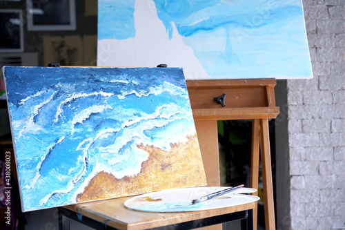 Acrylic sea and beach painting on drawing stand with palette and brush. Blue wave on golden sand hand painting with brush and knife palette technique. Art on canvas.