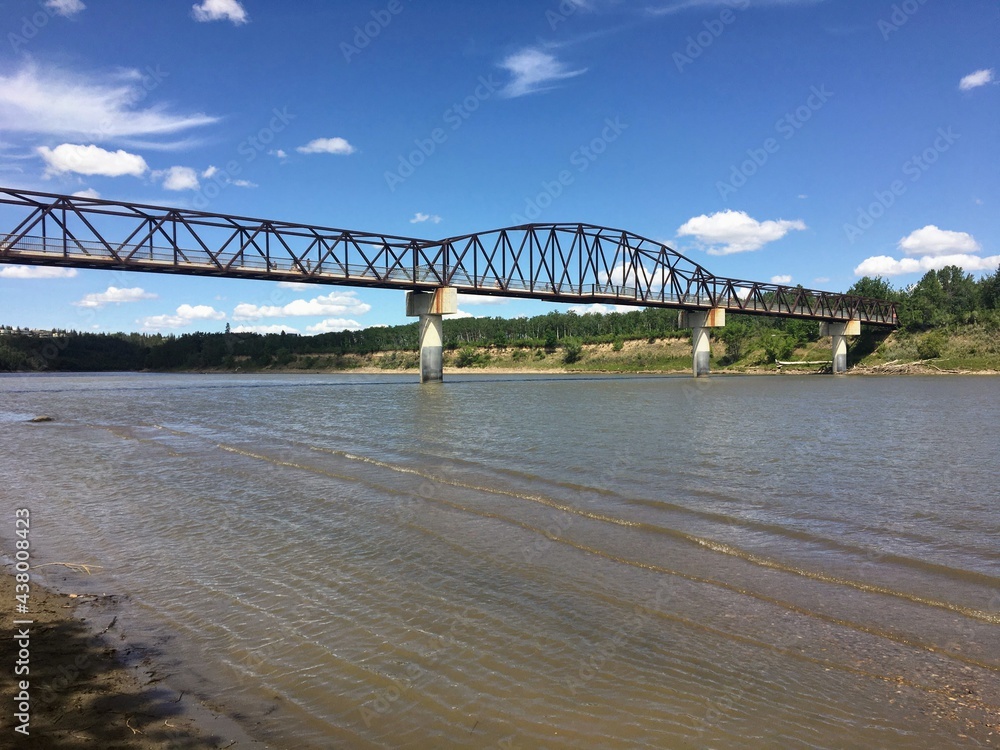 Obraz premium A view of a beautiful walking bridge crossing over a river from the perspective of the beach down below. This is a bridge along with north saskatchewan river in Edmonton, Alberta, Canada