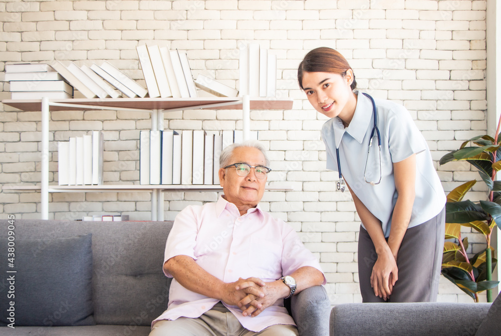 Fototapeta premium senior man at the nursing home concept. Nurse is with an elderly man sitting on armchair in living room at the care center nursing home looking at camera and smile