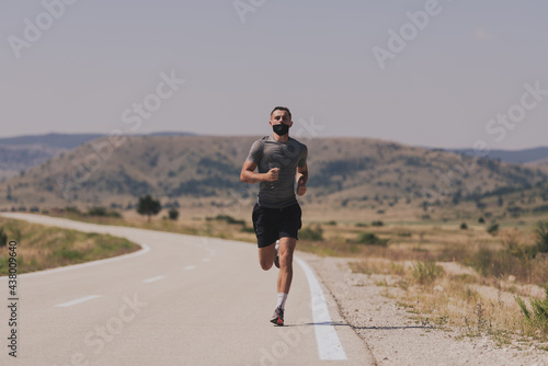 Fototapeta Naklejka Na Ścianę i Meble -  Young man and woman in protective masks running and doing exercises outdoors in the morning. Sport, Active life Jogging during quarantine. Covid-19 new normal. High quality photo. Selective focus.
