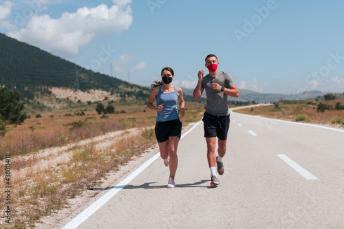 Young man and woman in protective masks running and doing exercises outdoors in the morning. Sport, Active life Jogging during quarantine. Covid-19 new normal. Selective focus.