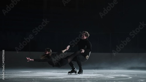 Slow motion: young couple of artistic figure skaters is performing a pair skating choreography on ice rink before start of a competition. Concept of perfection, precision, freedom, passion