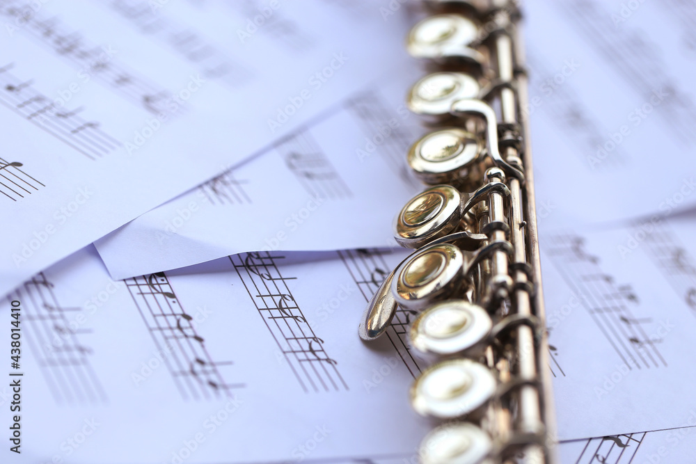 Fototapeta premium Flute, woodwind brass instrument in classical orchestra. Silver modern flute on white sheet music note for education and performance. Song composer on score sheet for orchestra.