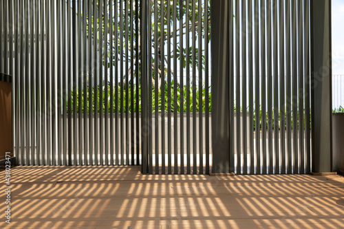 modern architectural shaded garden indoor outdoor area with vertical slats casting strong shadows on timer decking floor. A frangipani tree can be seen through the screen.