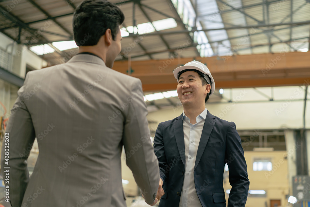 30s young Asian businessman in formal suit and hard hat showing foreign business partner in factory background. Business partnership and team work success concept - 4K Real Time Footage 30s young Asian businessman in formal suit and hard hat showing foreign business partner in factory background. Business partnership and team work success concept - 4K Real Time Footage