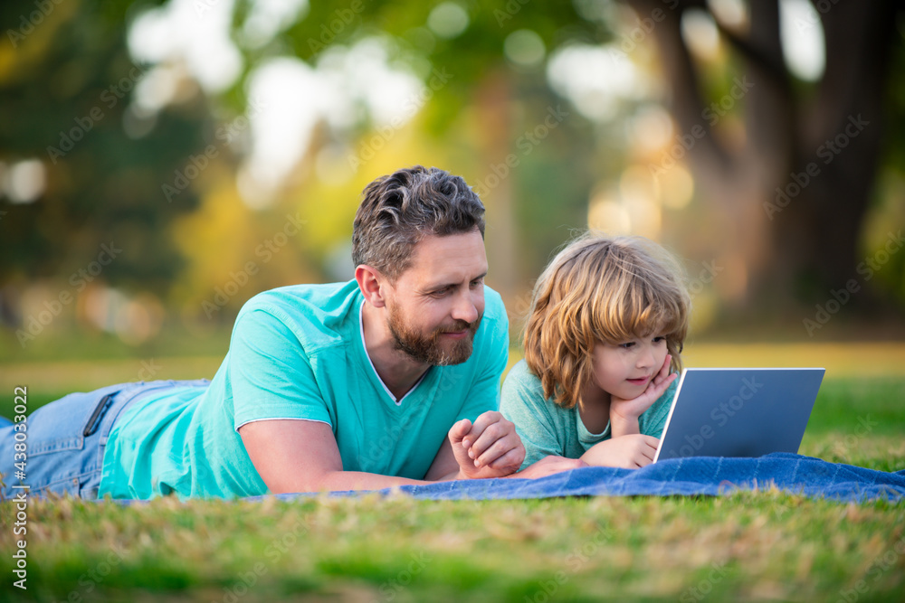 Happy father using laptop relax with schooler son holding laptop have fun together, smiling dad and little boy child enjoy weekend with gadgets outside on nature. Happy father using laptop relax with schooler son holding laptop have fun together, smiling dad and little boy child enjoy weekend with gadgets outside on nature.