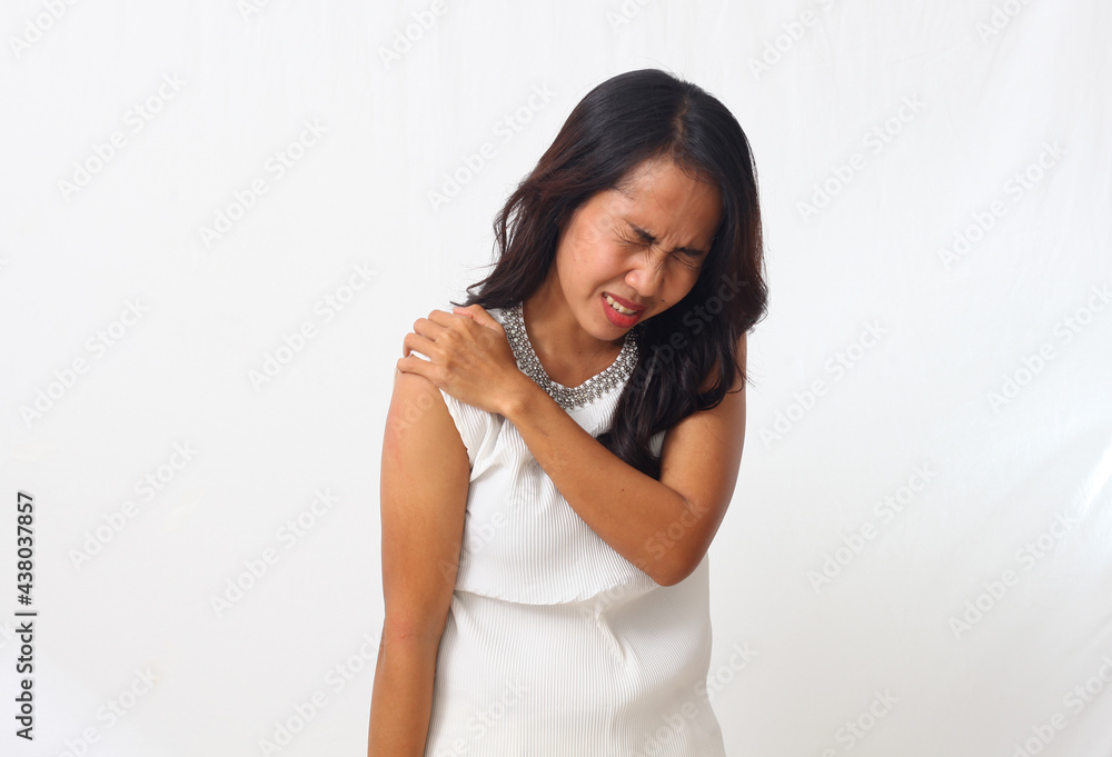 Beautiful asian girl standing while holding and feeling pain in her shoulder. Isolated on white background with copyspace Beautiful asian girl standing while holding and feeling pain in her shoulder. Isolated on white background with copyspace