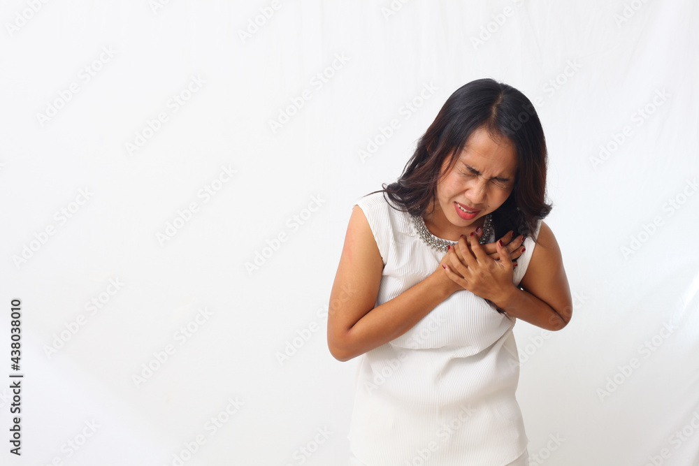 Close up photo of asian woman over isolated white background having a pain in the heart or chest pain or heart attack Close up photo of asian woman over isolated white background having a pain in the heart or chest pain or heart attack