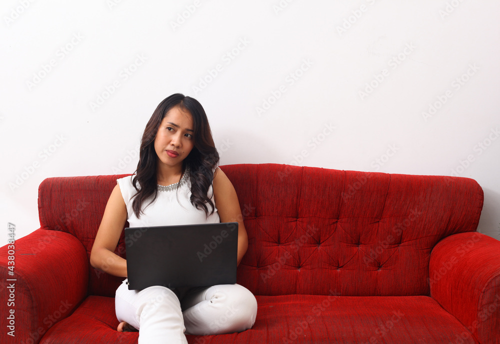Asian woman using a laptop while sitting on red sofa.Asian woman using a laptop while sitting on red sofa. Work from home concept Asian woman using a laptop while sitting on red sofa.Asian woman using a laptop while sitting on red sofa. Work from home concept