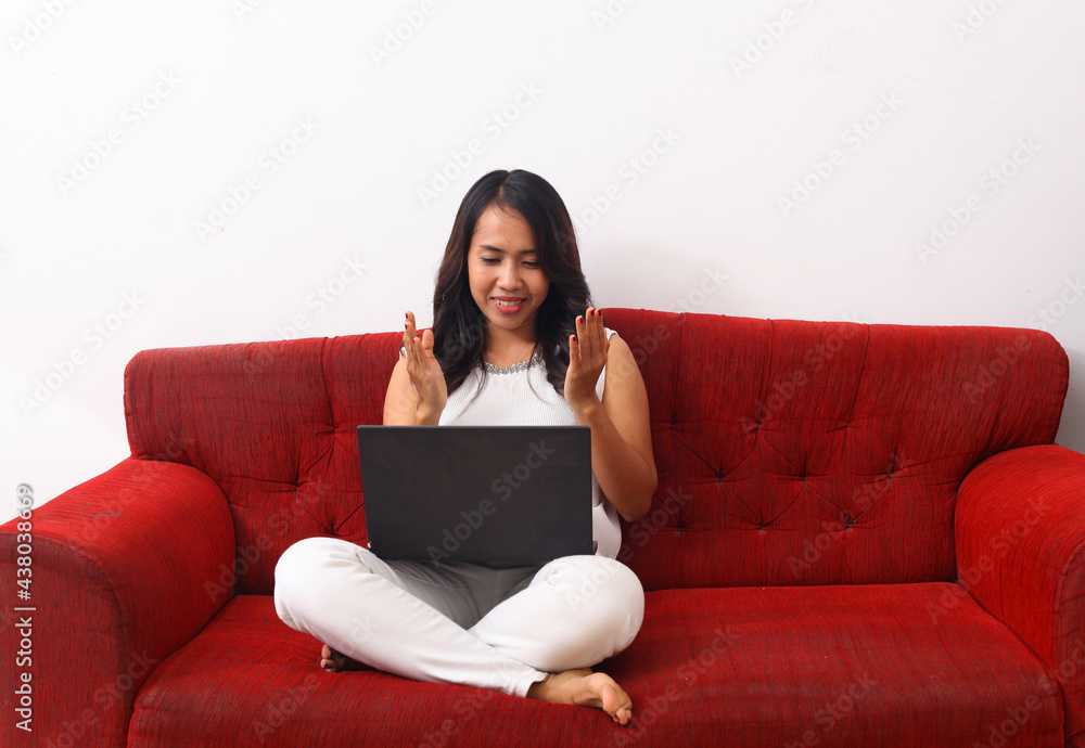 Happy Asian woman using a laptop while sitting on red sofa. Happy Asian woman using a laptop while sitting on red sofa.