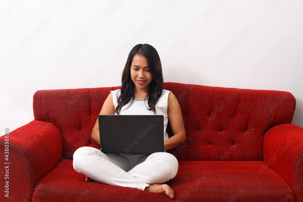 Happy Asian woman using a laptop while sitting on red sofa. Online meeting concept