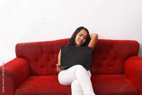 Asian woman using a laptop while sitting on red sofa.