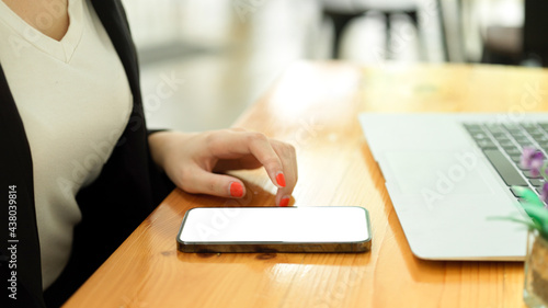 Side view of smartphone with mock-up screen on wooden desk with laptop