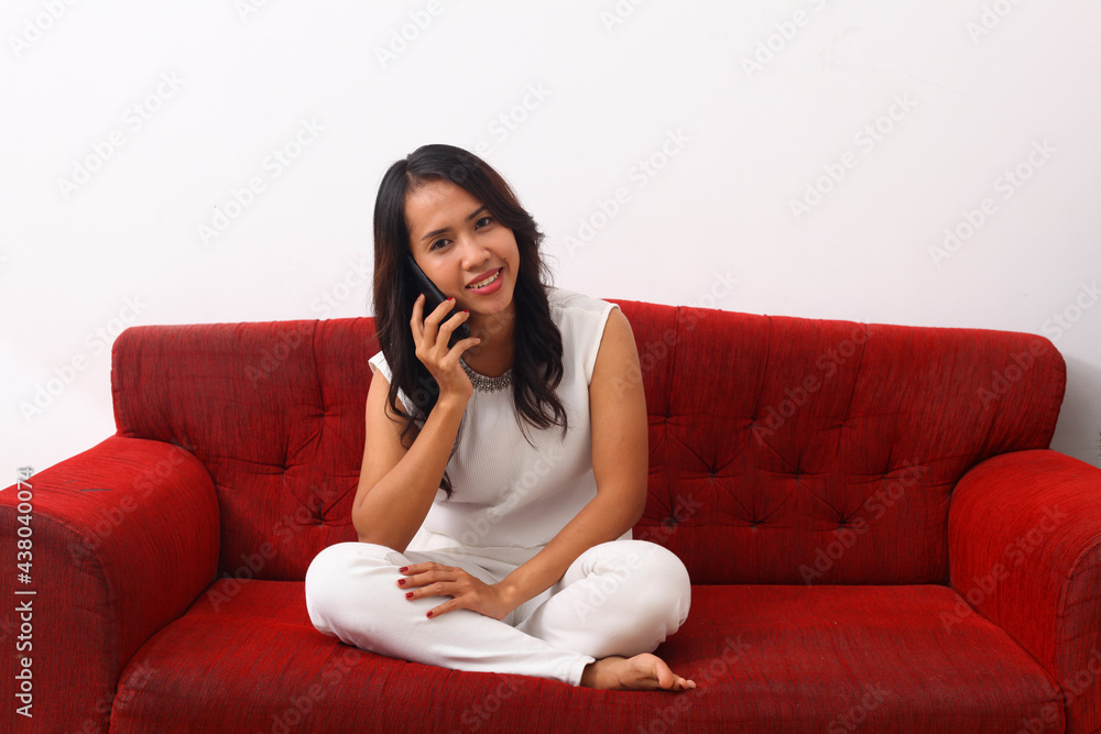 Asian woman using mobile phone while sitting on red sofa Asian woman using mobile phone while sitting on red sofa
