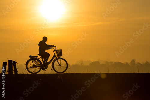 The Girl riding the bicycle during the morning with the background of sunrise in summer. The girl feeling happiness with her lifestle to exercise before going to school