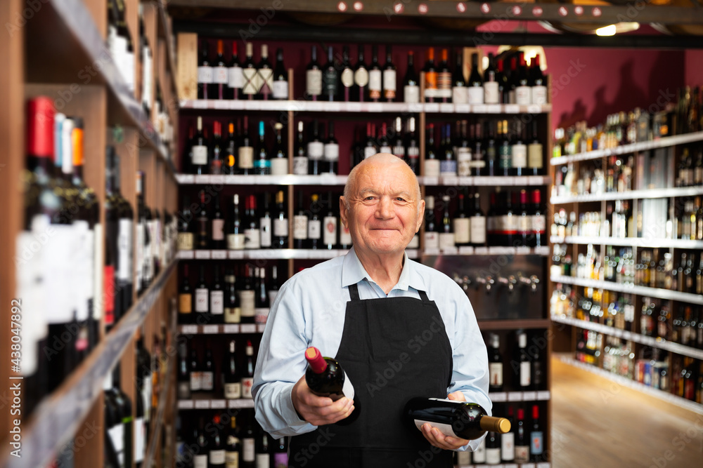 Smiling grey-haired senior vintner offering wine in modern wineshop