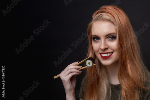 Portrait of smiling attractive white teeth young woman tasting sushi by wooden sticks  looking at the camera. Horizontally. 