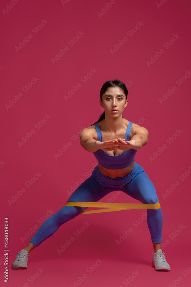 Girl doing lateral lunges with resistance band on maroon background Girl doing lateral lunges with resistance band on maroon background