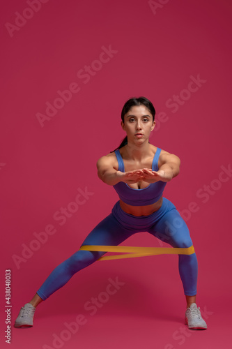 Girl doing lateral lunges with resistance band on maroon background