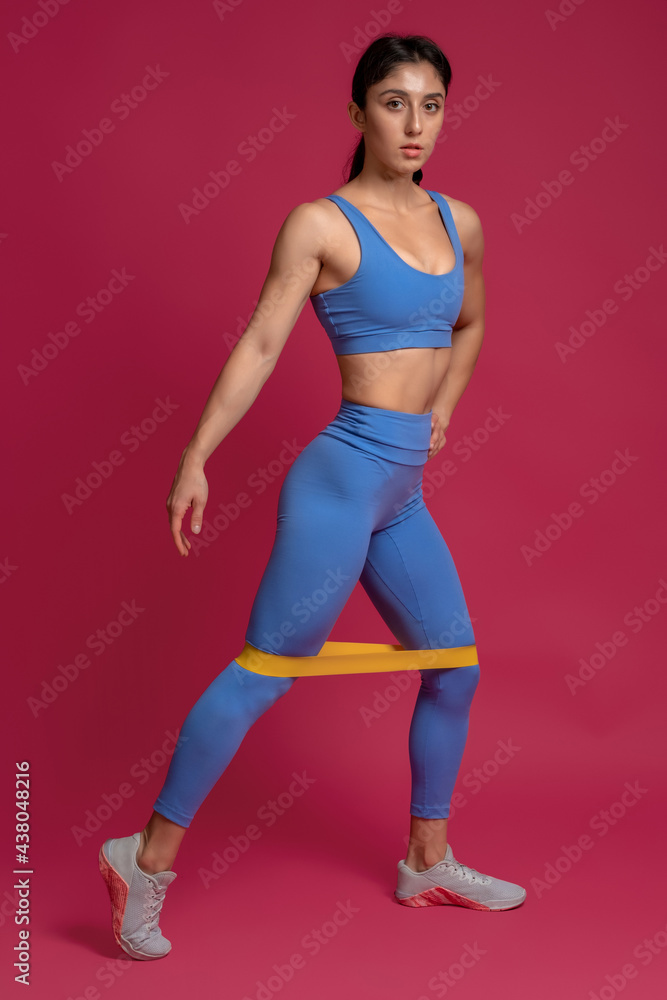 Girl doing lower body exercises with resistance band on maroon background
