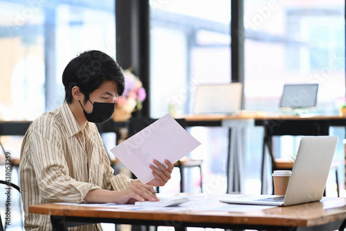 Young man office worker in protective mask analyzing business data at office desk.