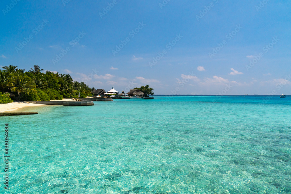 Scenic  landscape of Maldives beach and pier with speed boats and yachts on the horizon. Seascape with water bungalows, beautiful turquoise sea and lagoon waters, tropical nature paradise. 