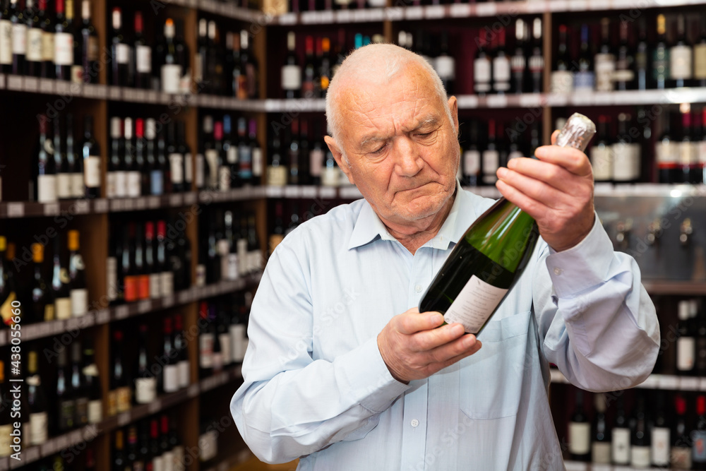 Older man looking for perfect champagne for solemn occasion in wine store. High quality photo