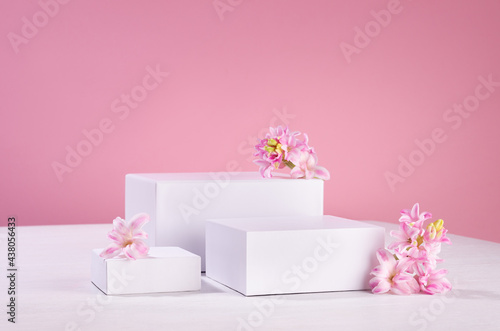 Three different square white podiums for display cosmetic produce or goods with fresh spring flowers and soft light pastel pink background. © finepoints