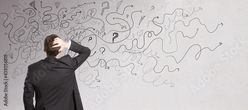 Pensive businessman with abstract arrows sketch on concrete wall background. Confusion and direction concept. photo