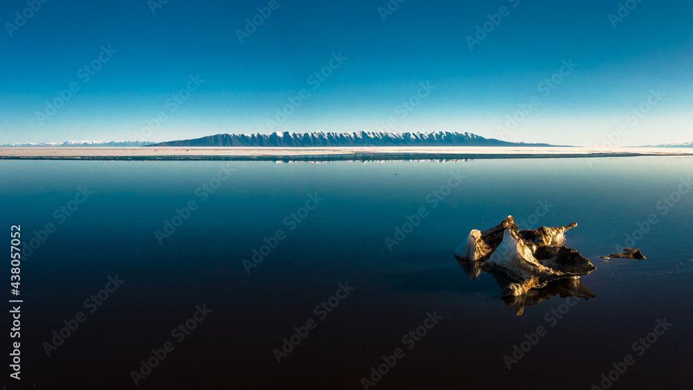 Naklejka premium minimalistic view of seascape with melting ice on foreground and mountain range on background with blue sky reflected in water at daylight