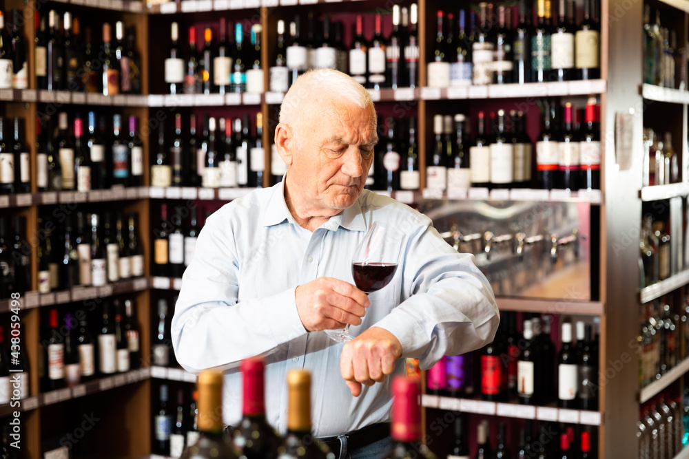 Portrait of senior man tasting red wine at wine shop. High quality photo