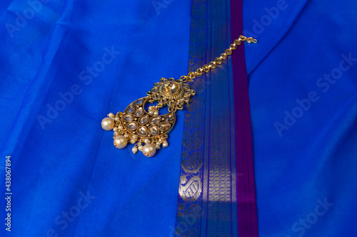 Indian traditional gold Indian wedding women's jewelry tikka on blue saree background. Close-up. Still-life.