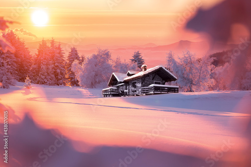 Golden sunlight over a idyllic white winter landscape with a little wooden hut in background