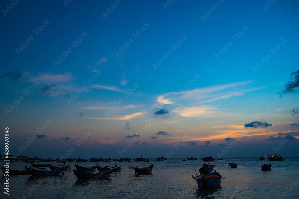 Beautiful sunset tropical beach with small boat and pink sky and ocean waves on a tropical sea at Vung Tau. Tropical Seascape with a boat on sandy beach at cloudy sunrise or sunset.
