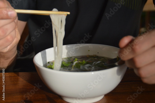 Person eating a bowl of traditional Lao beef rice noodle soup called Feu