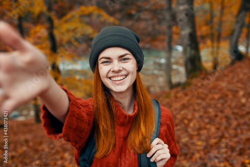 energetic woman tourist with a backpack in a red sweater and caps are resting in the autumn forest in the park