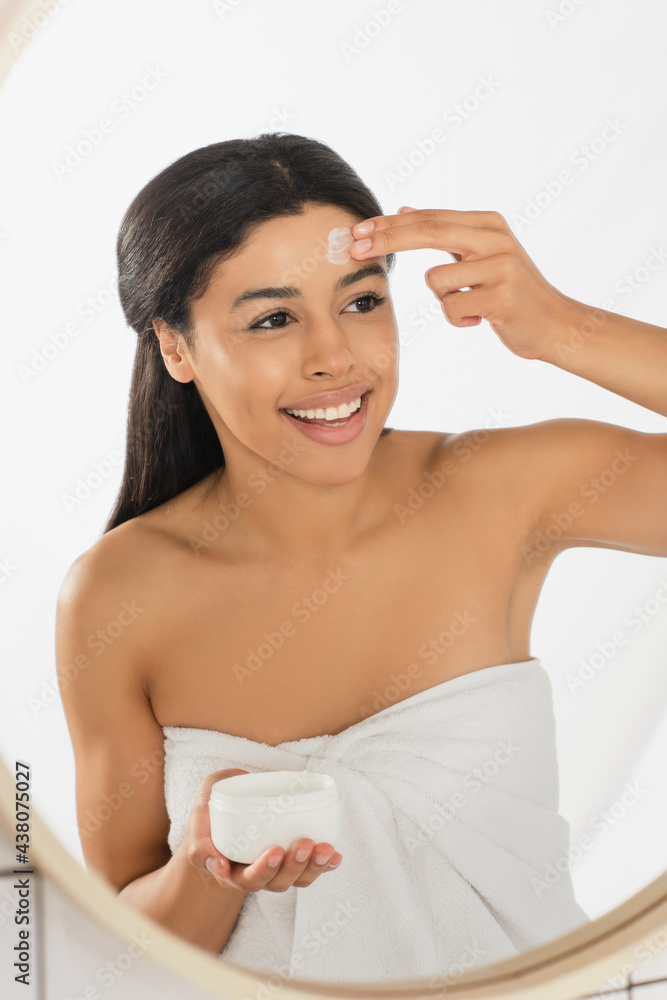 young african american woman wrapped in towel applying cream on face in bathroom young african american woman wrapped in towel applying cream on face in bathroom