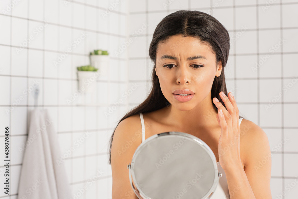 worried young african american woman looking in mirror and holding hand near face in bathroom worried young african american woman looking in mirror and holding hand near face in bathroom