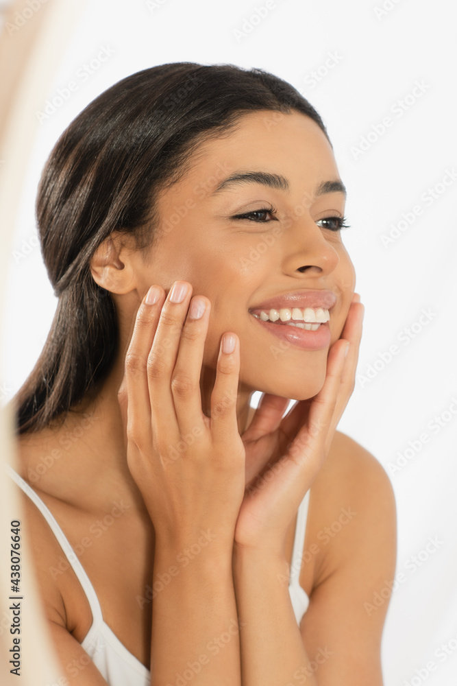 positive young african american woman looking in mirror with hands near face on white background positive young african american woman looking in mirror with hands near face on white background